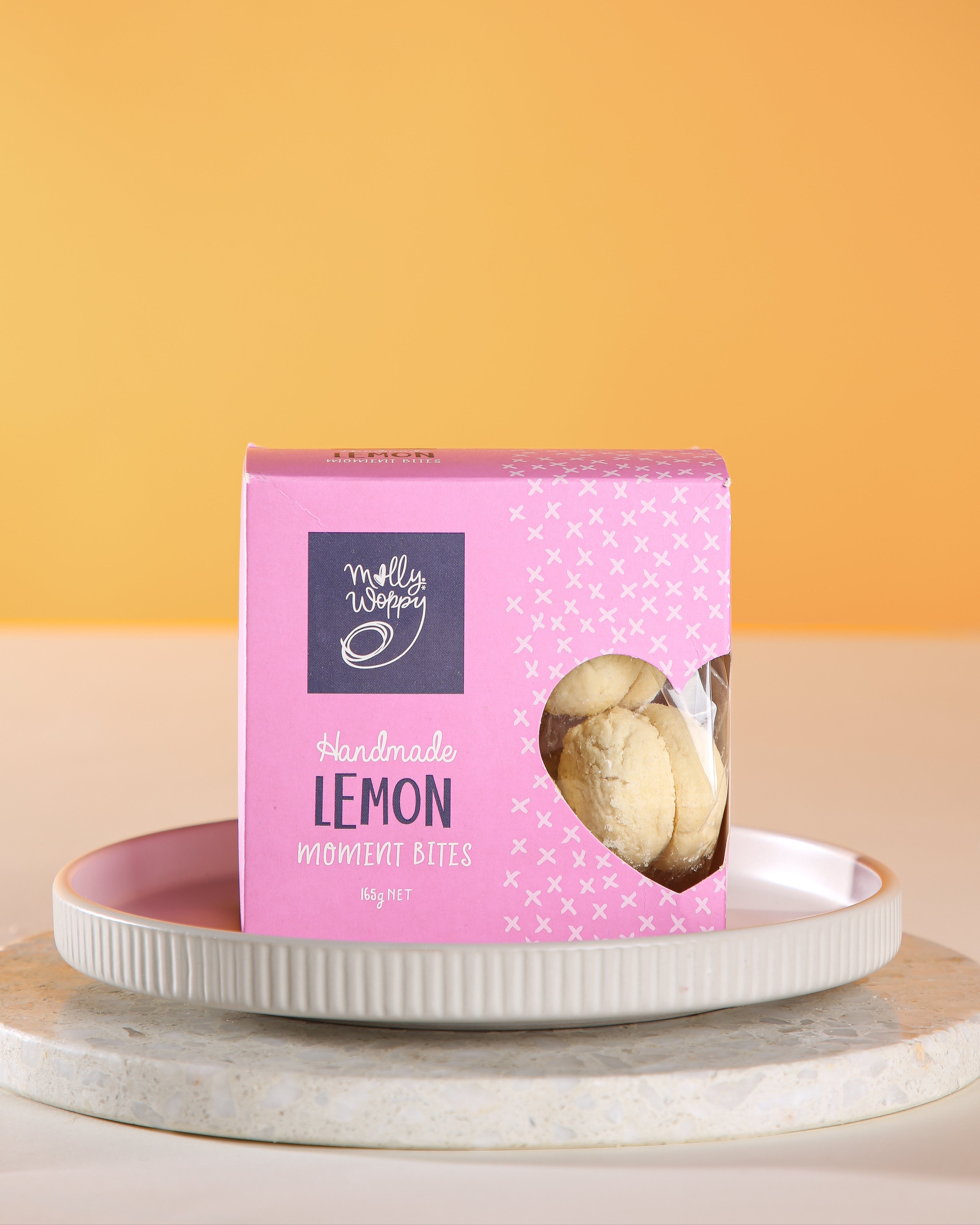 Pink box of lemon cookies on a white plate with a yellow background