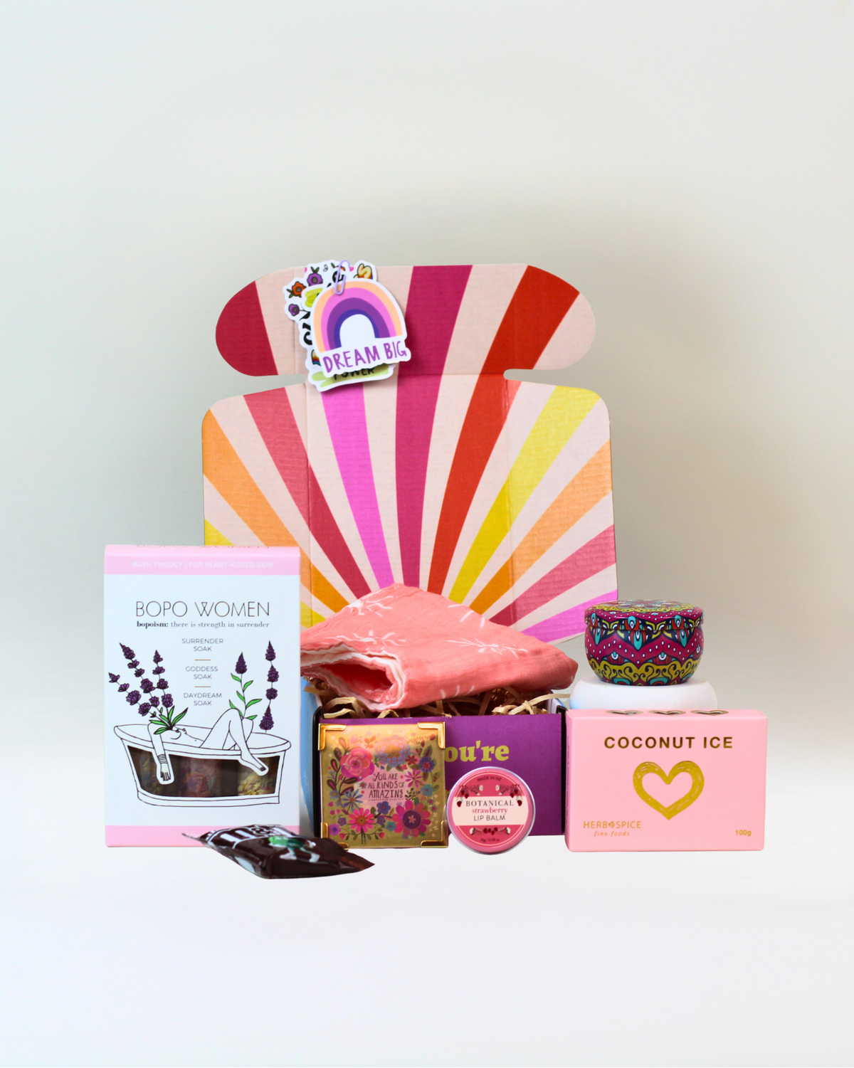 Wellness gift box NZ | Pamper box with bath salts trio, pink clay mask, cotton facecloth, hand-poured candle, keepsake magnet, M&M’s and coconut ice. A cheerful self-care gift.