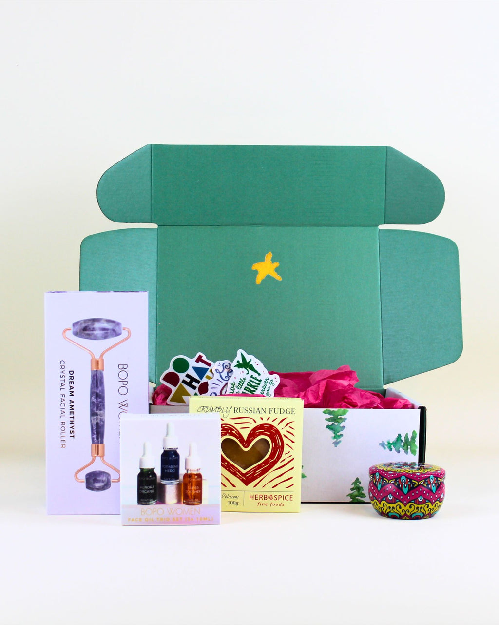 “Christmas gift box with Bopo Women amethyst crystal facial roller, facial oil trio, Herb & Spice Russian fudge, and scented mandala candle.”