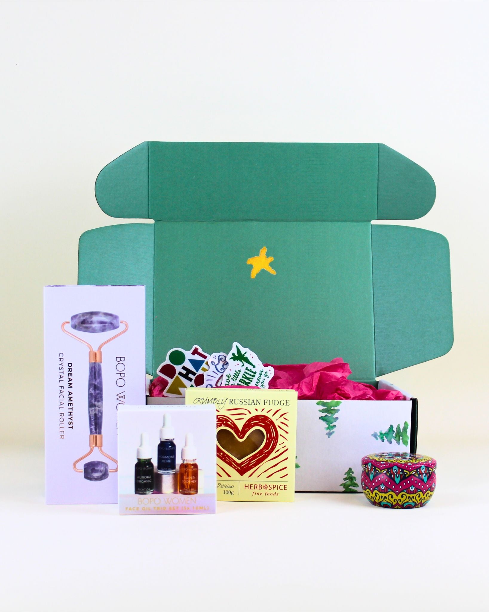“Christmas gift box with Bopo Women amethyst crystal facial roller, facial oil trio, Herb & Spice Russian fudge, and scented mandala candle.”