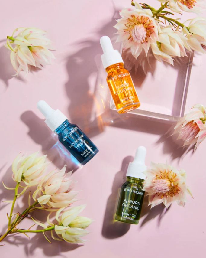 Three skincare serum bottles on a pink surface with flowers around them