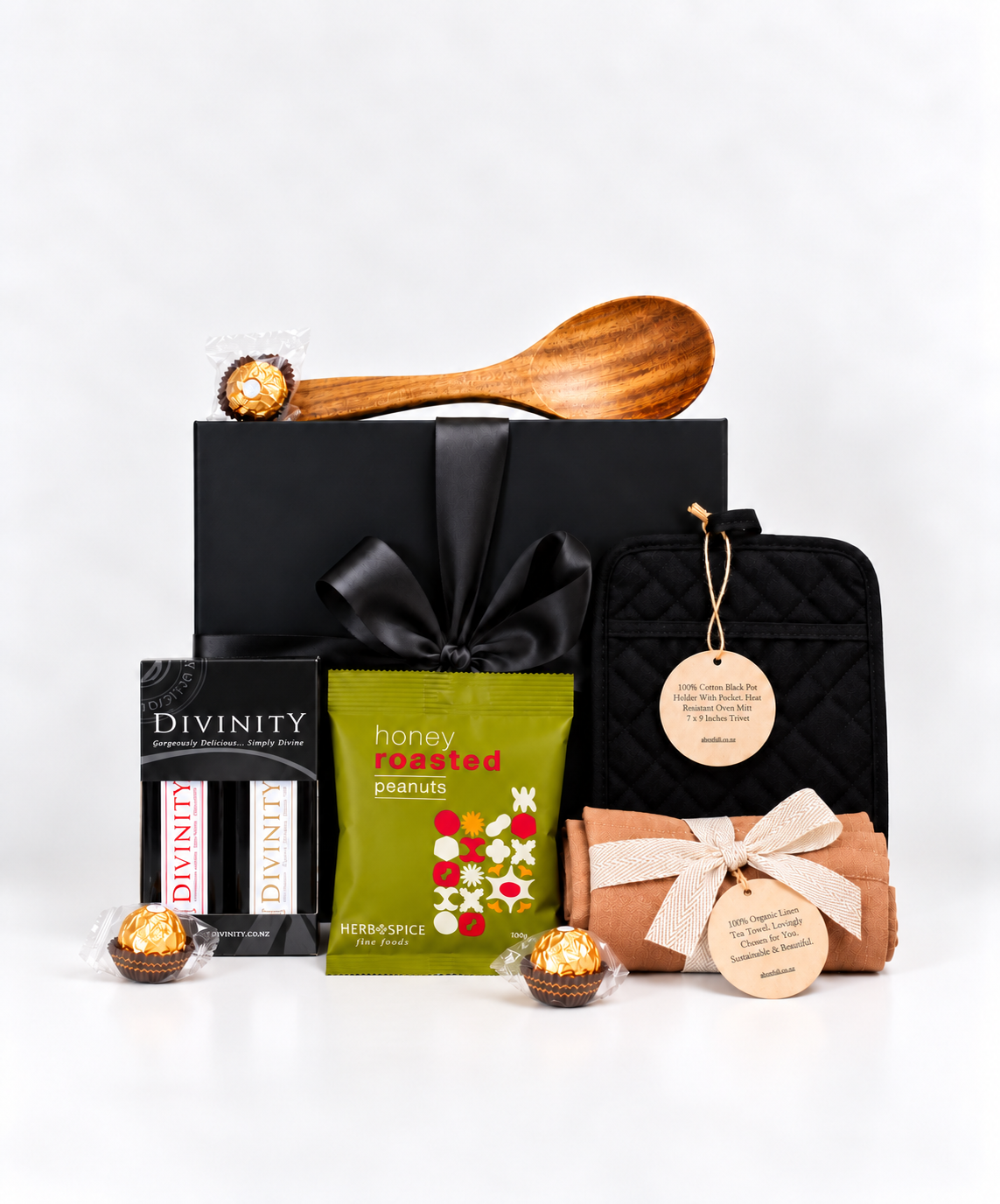 Premium kitchen and gourmet gift box NZ featuring a black magnetic gift box with satin bow, wooden serving spoon, Divinity olive oil and balsamic vinegar set, honey roasted peanuts, organic linen tea towel, black oven mitt and Ferrero Rocher chocolates. Beautifully presented for housewarming, thank you and special occasion gifting.
